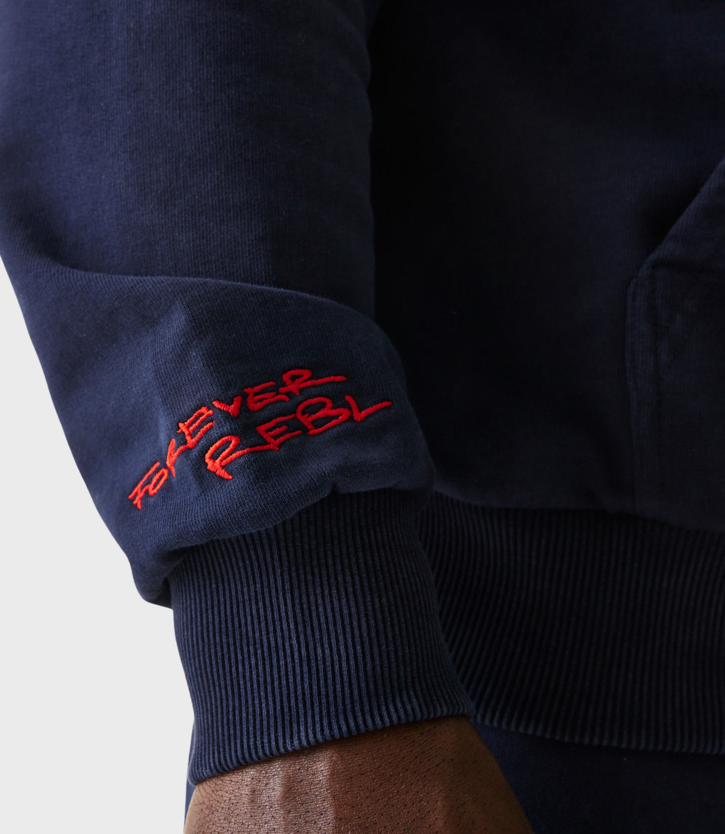 Close up of navy oversized hoodie sleeve with red REBL embroidery near the cuff