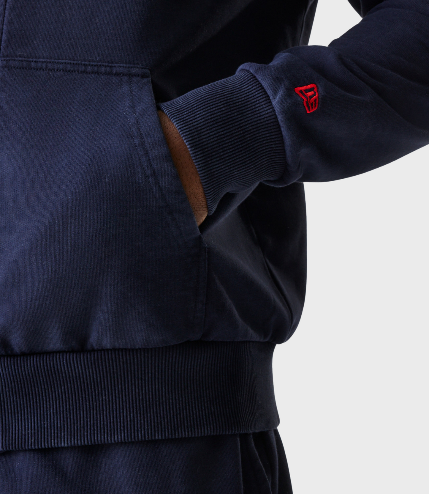 Back view of a person wearing a navy oversized hoodie and a black cap with a red adjustable strap