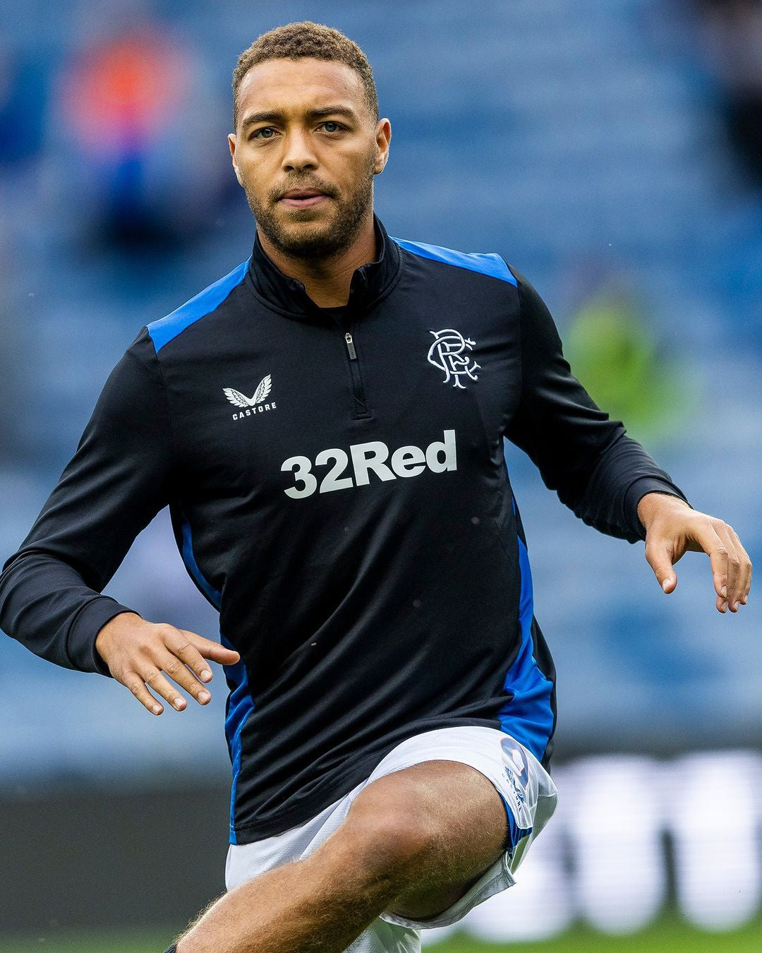 Male footballer wearing black and blue matchday training fleece with club crest and 32Red sponsor