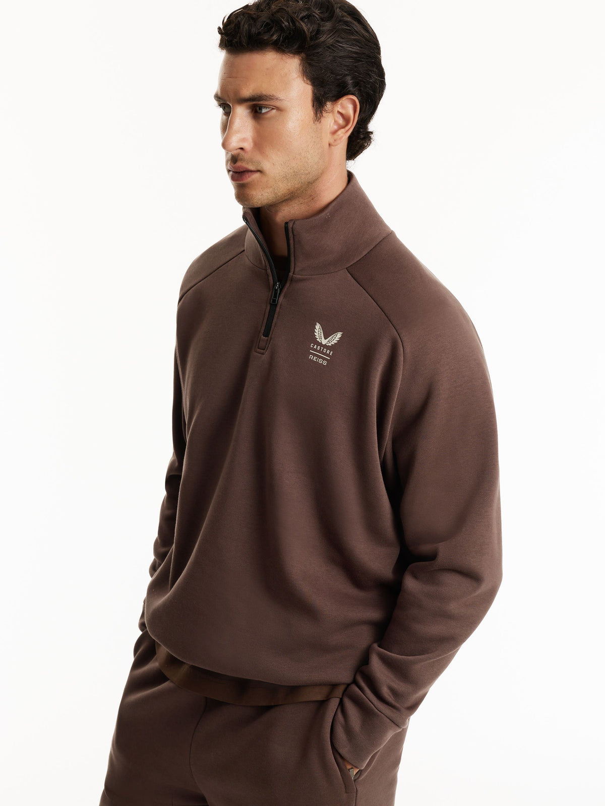 A man wearing a brown quarter-zip sweatshirt and matching sweatpants, photographed against a clean white studio background.
