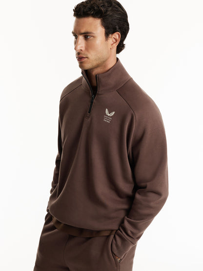A man wearing a brown quarter-zip sweatshirt and matching sweatpants, photographed against a clean white studio background.