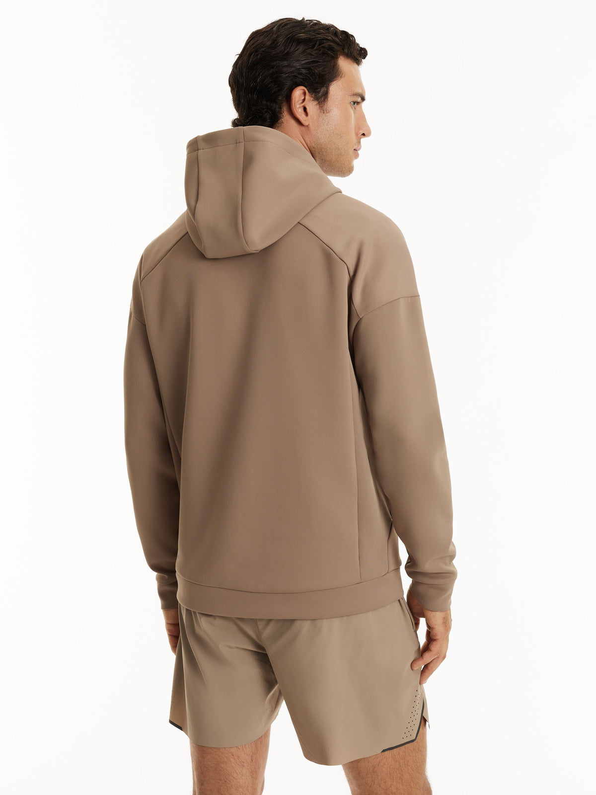 A man shown from the back wearing a taupe-brown hooded sweatshirt and matching shorts against a clean white studio background.