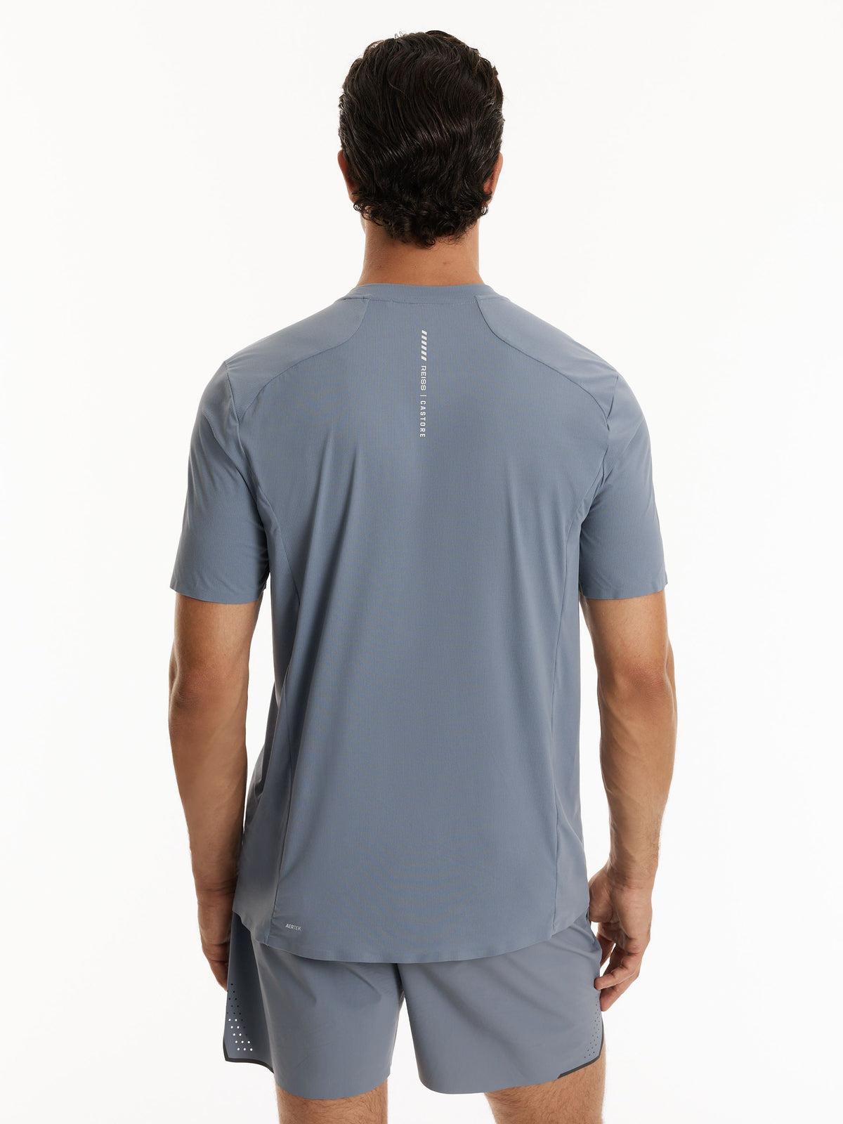 A man viewed from the back wearing a slate blue athletic t-shirt and matching shorts against a plain white background.