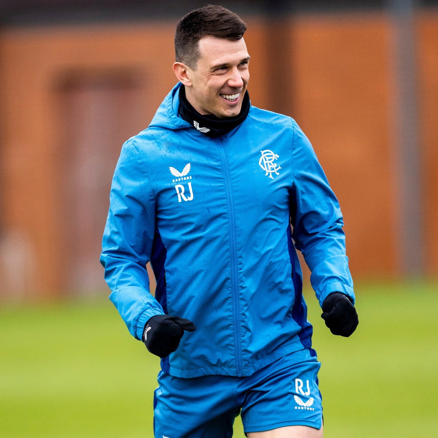 Athlete wearing bright blue training jacket with hood outdoors showing club crest on left chest and Castore branding