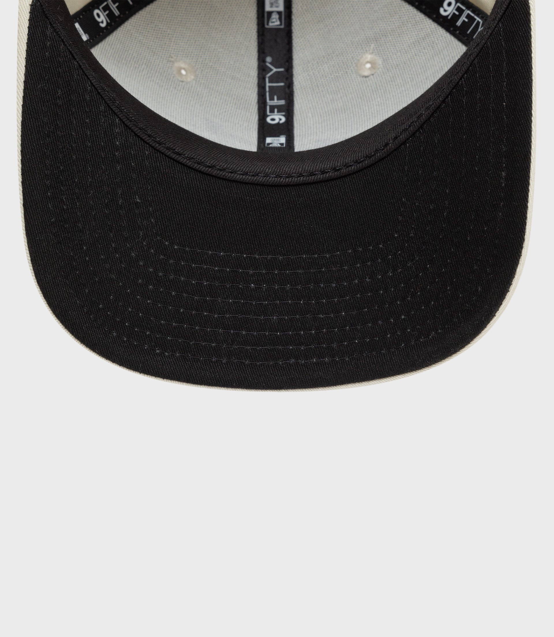 Close up of New Era Alpine 9Fifty pre curved cap in black with tan edge showing brim stitching and interior 9FIFTY branding