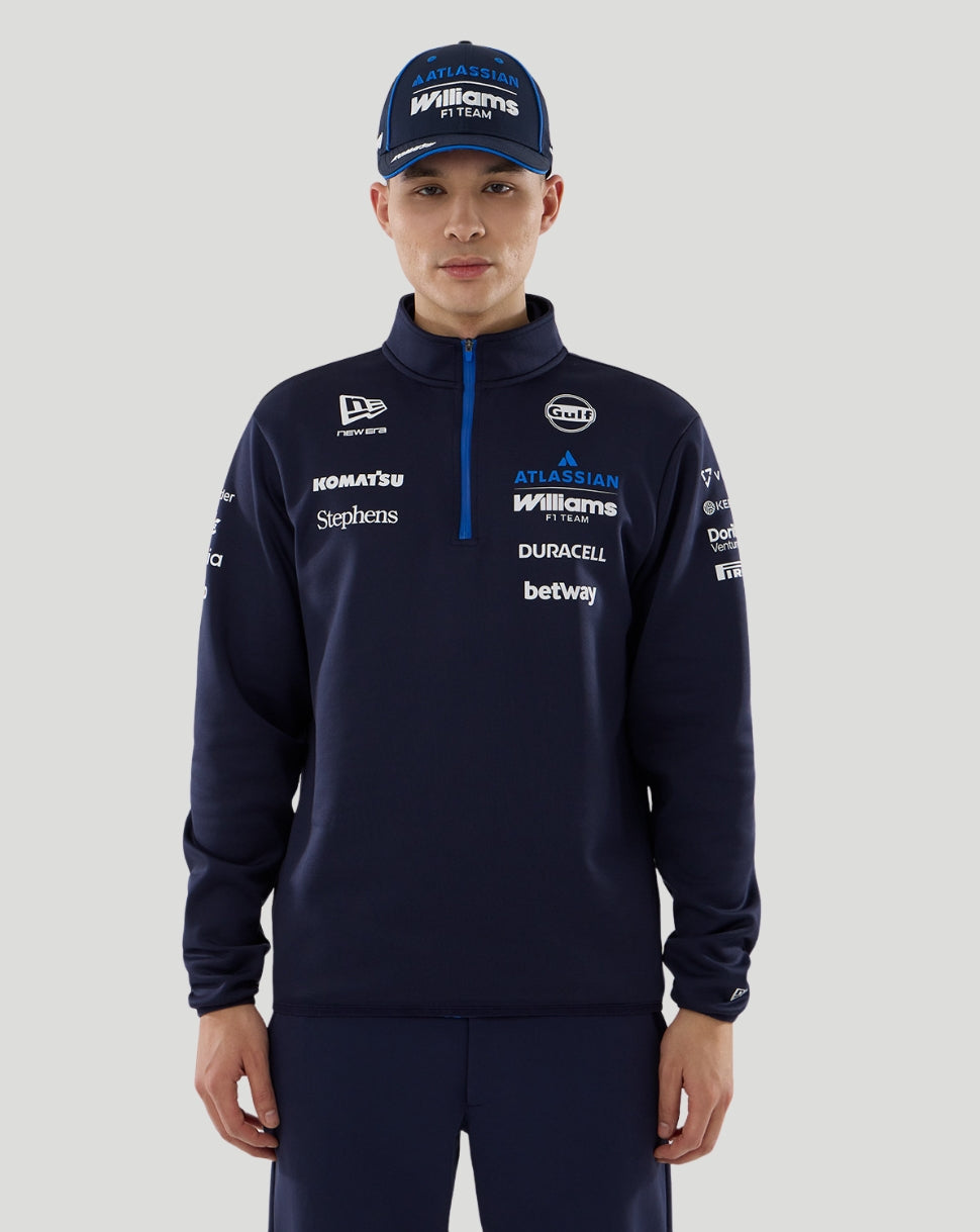 Person wearing a navy tracksuit with various sponsor logos on a gray background