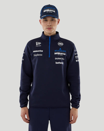 Person wearing a navy tracksuit with various sponsor logos on a gray background