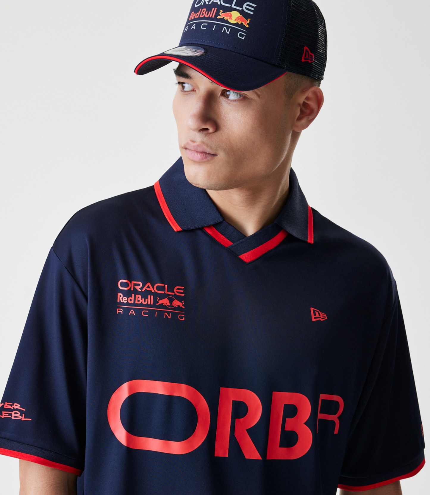 Close up of navy polo with red piping showing ORBR branding on chest and a New Era flag embroidery.