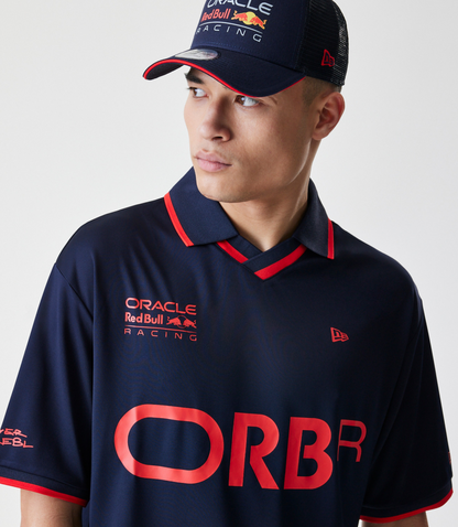 Close up of navy polo with red piping showing ORBR branding on chest and a New Era flag embroidery.