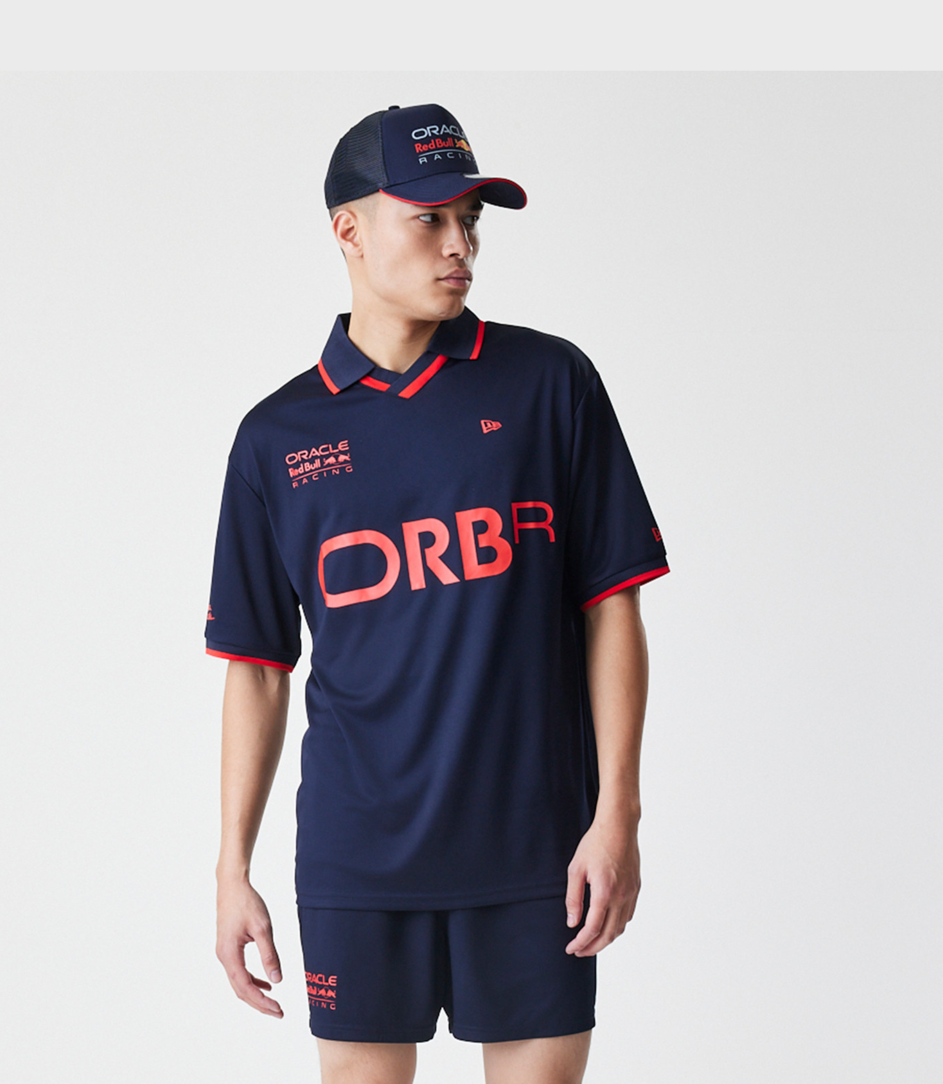 Male model wearing navy Red Bull Racing football jersey with large ORBR letters and cap featuring Oracle Red Bull Racing branding.