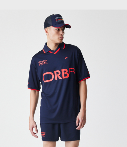 Male model wearing navy Red Bull Racing football jersey with large ORBR letters and cap featuring Oracle Red Bull Racing branding.