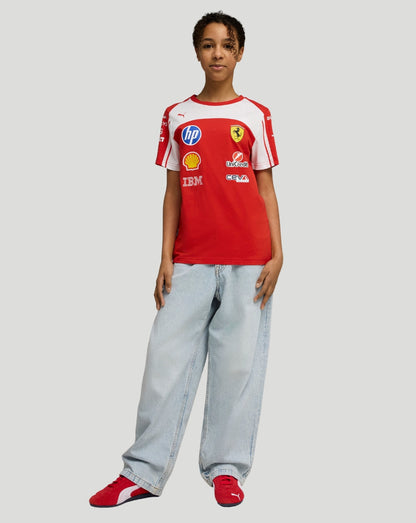 Front view of a young girl wearing a red and white Scuderia Ferrari junior team T shirt with sponsor logos on the chest.