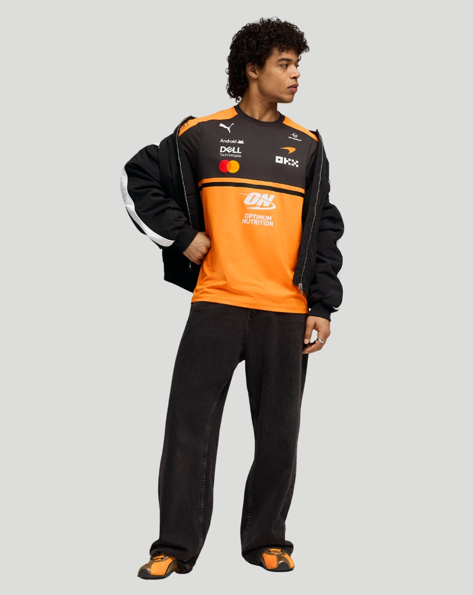 Side view of a model wearing the Papaya McLaren team T-shirt with orange panels and sponsor logos under a black jacket