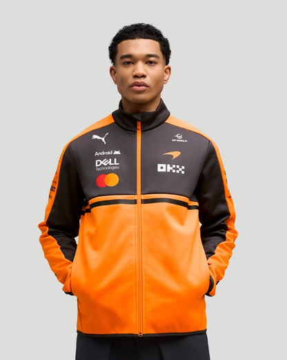 Male model in a papaya and charcoal McLaren team softshell jacket with multiple logos on the chest.