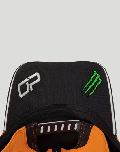 Close up of black Papaya McLaren cap with white Oscar Piastri initials and green Monster energy logo.
