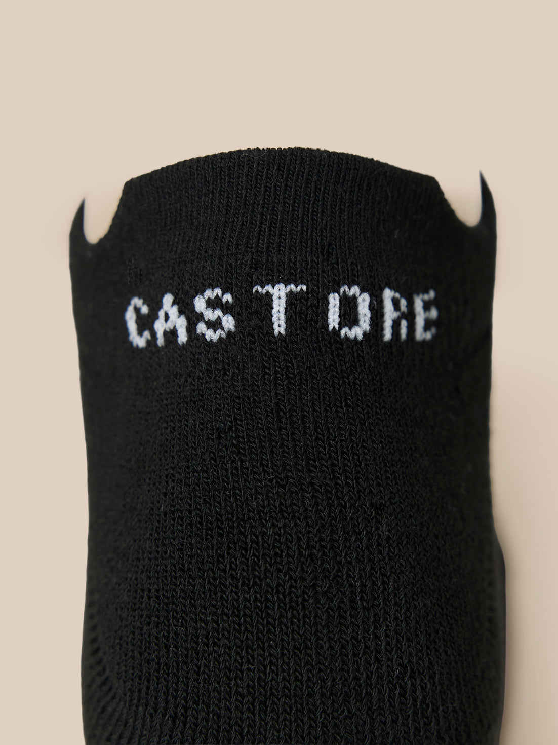 Close-up of a black Castore X Millburn trainer liner sock with white logo lettering