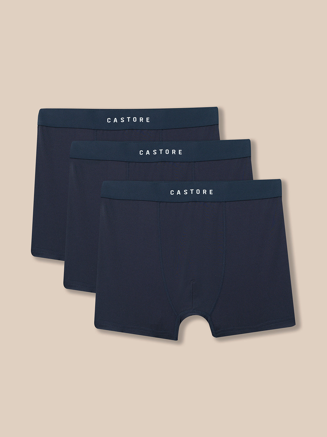 Three pairs of Castore men's boxer briefs in a dark navy blue color, arranged in a staggered stack on a solid beige background.