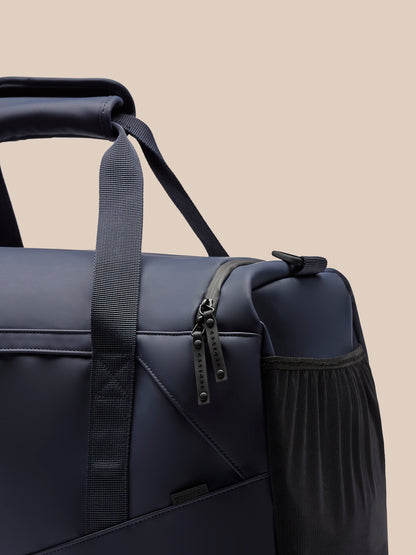 Close-up of navy Core Holdall zipper area showing dual pulls and a side mesh pocket