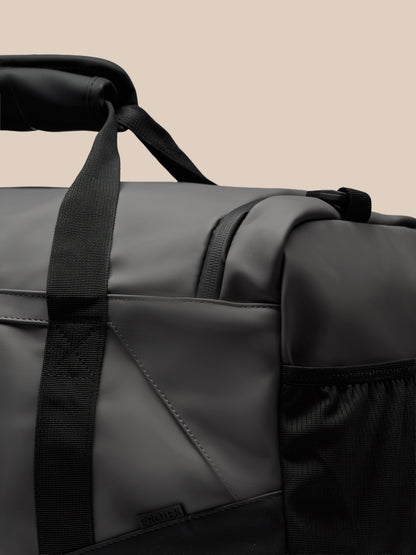 Male model in a blue gray shirt holds a large gunmetal and black Core Holdall with an adjustable strap across his body