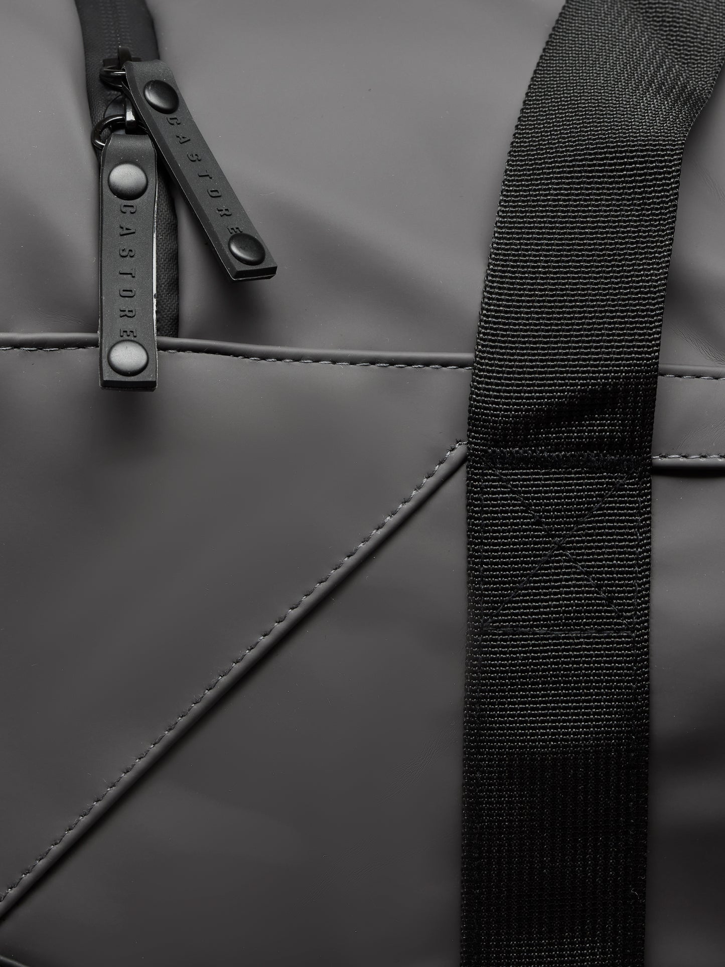 Close-up of Core Holdall in gunmetal black showing strap and branded zipper pulls on the bag surface
