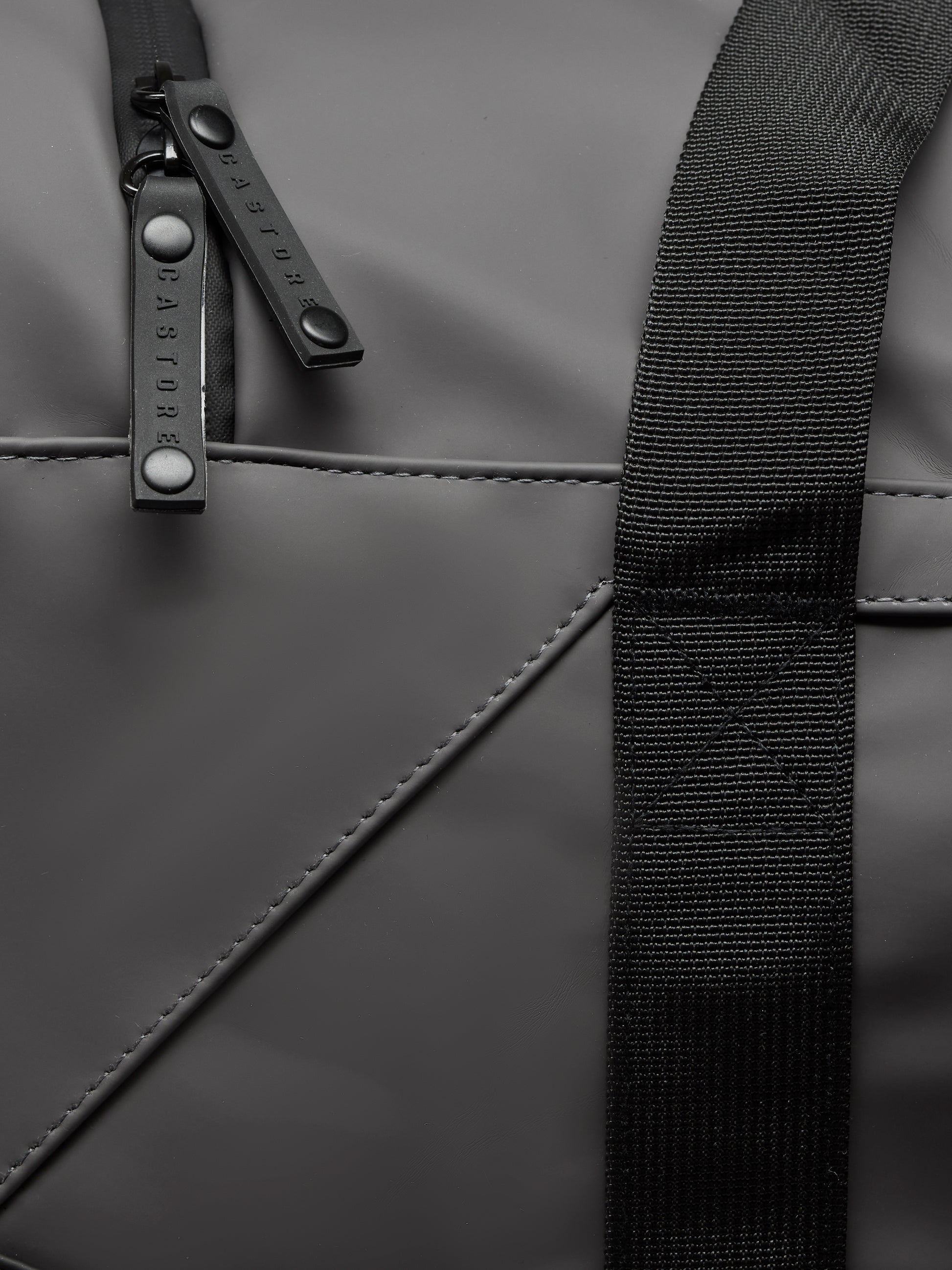 Close-up of Core Holdall in gunmetal black showing strap and branded zipper pulls on the bag surface
