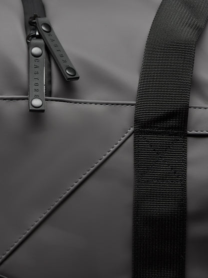 Close-up of Core Holdall in gunmetal black showing strap and branded zipper pulls on the bag surface
