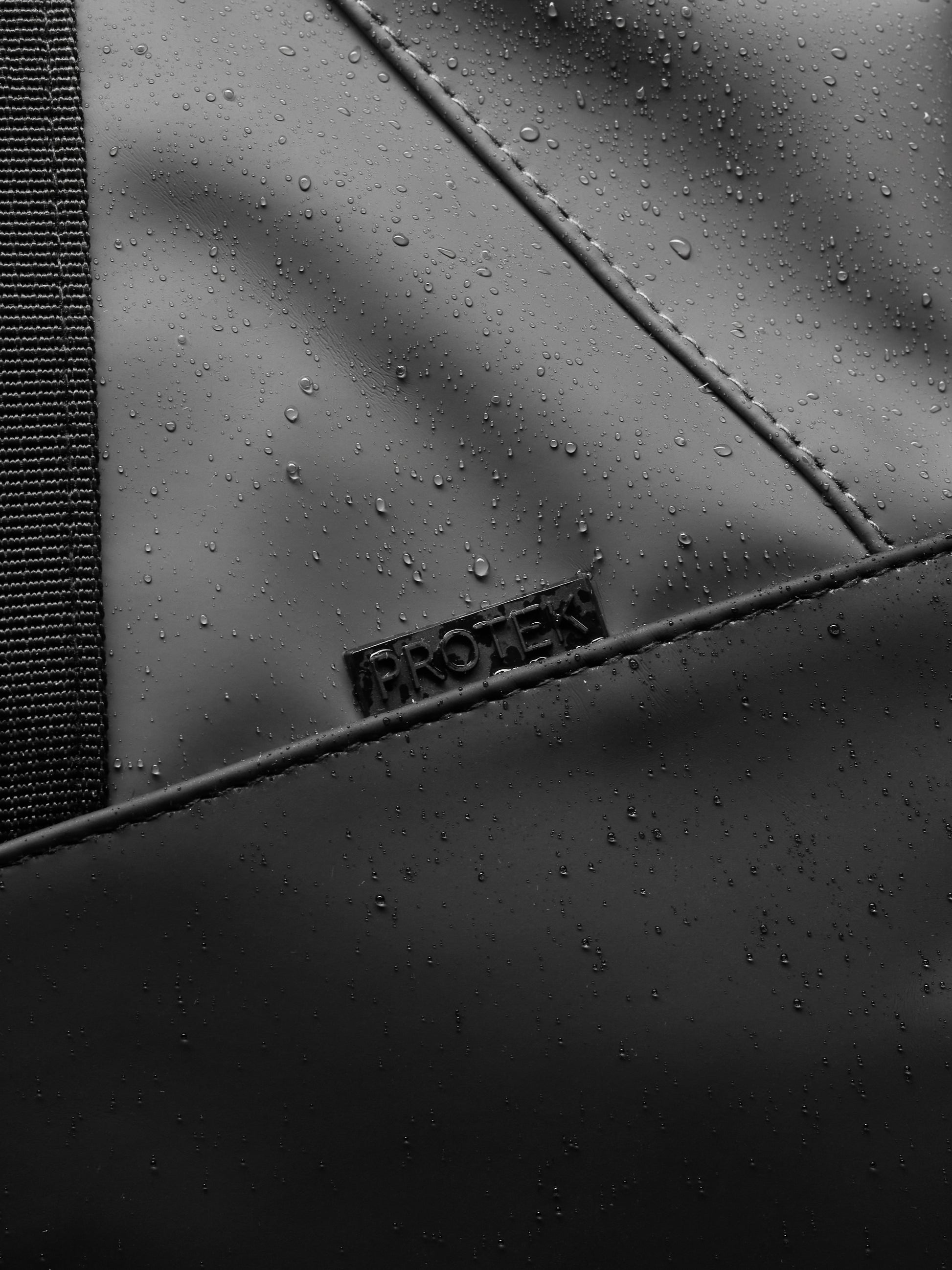 Close-up of Core Holdall gunmetal black polyurethane surface with water droplets and a woven strap.