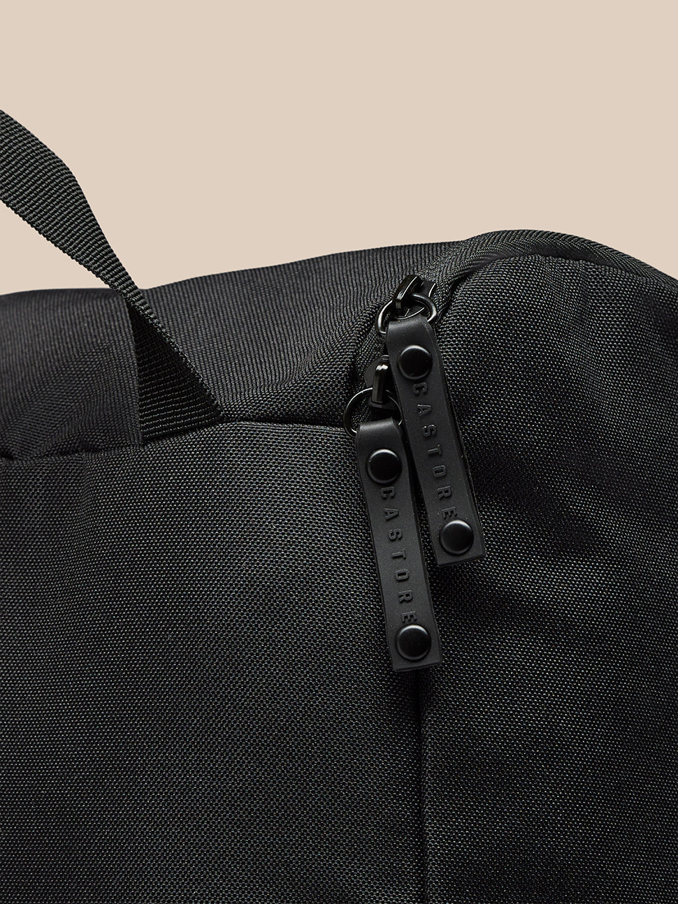 Close-up of black boot bag zipper area with two parallel zippers and Castore branding on textured fabric