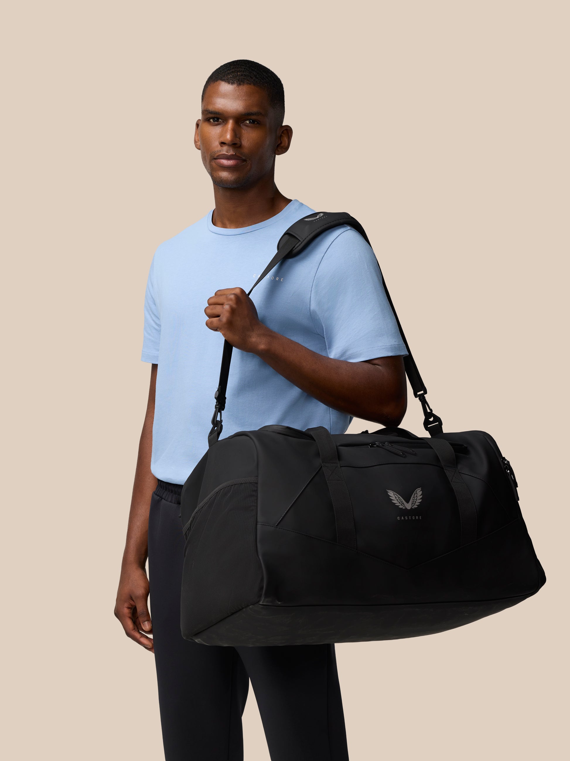 Man models a black Core Holdall with a crossbody strap and visible logo.