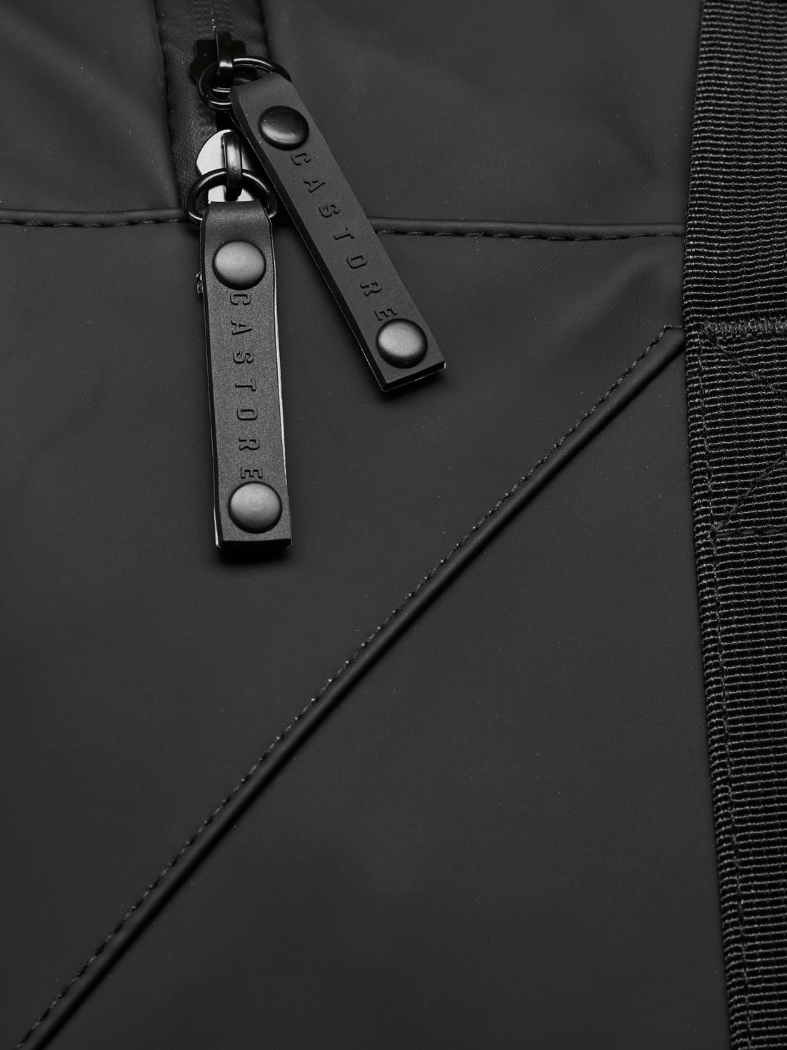 Close-up of black holdall zipper pulls on durable material with reinforced stitching and a woven strap edge