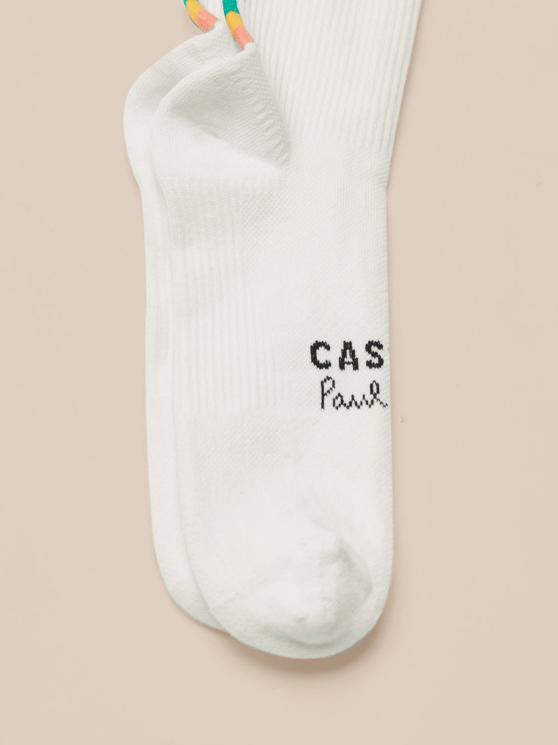 White Castore x Paul Smith technical sock with a multicolor striped cuff and dark branding near the toe area.