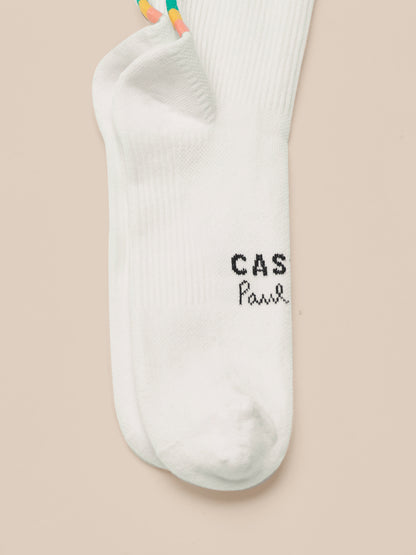 White Castore x Paul Smith technical sock with a multicolor striped cuff and dark branding near the toe area.