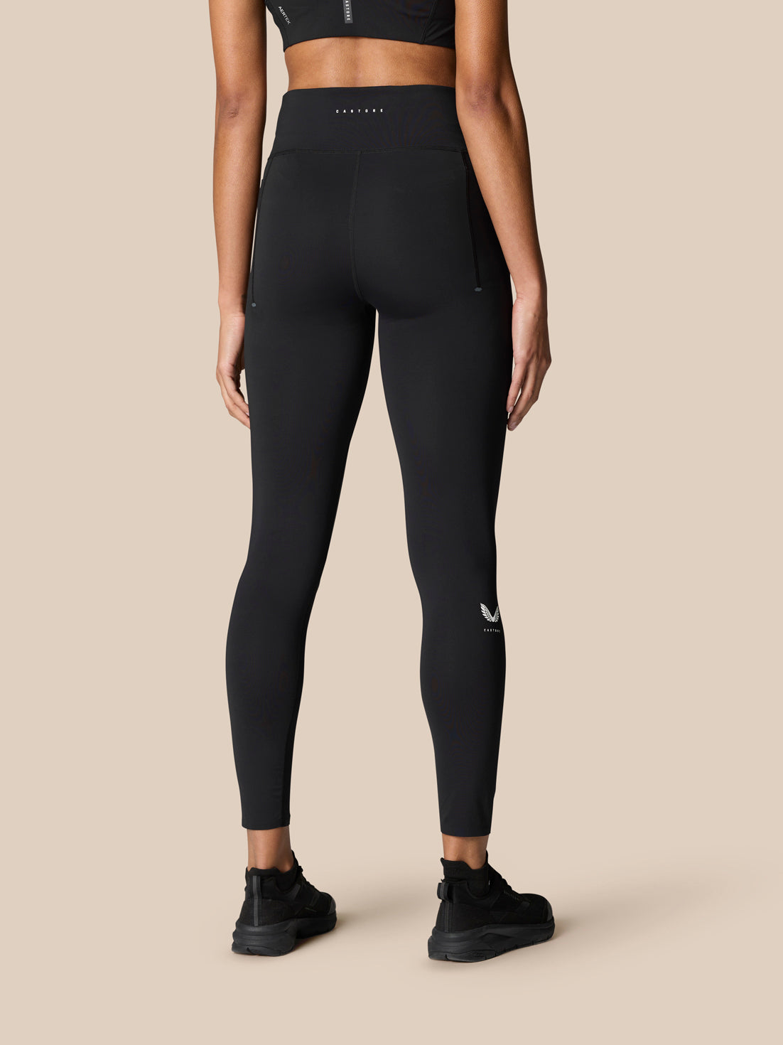 Back view of a model in black Zone full length training leggings with a high waistband and Castore branding on the waistband and a small logo on the lower leg
