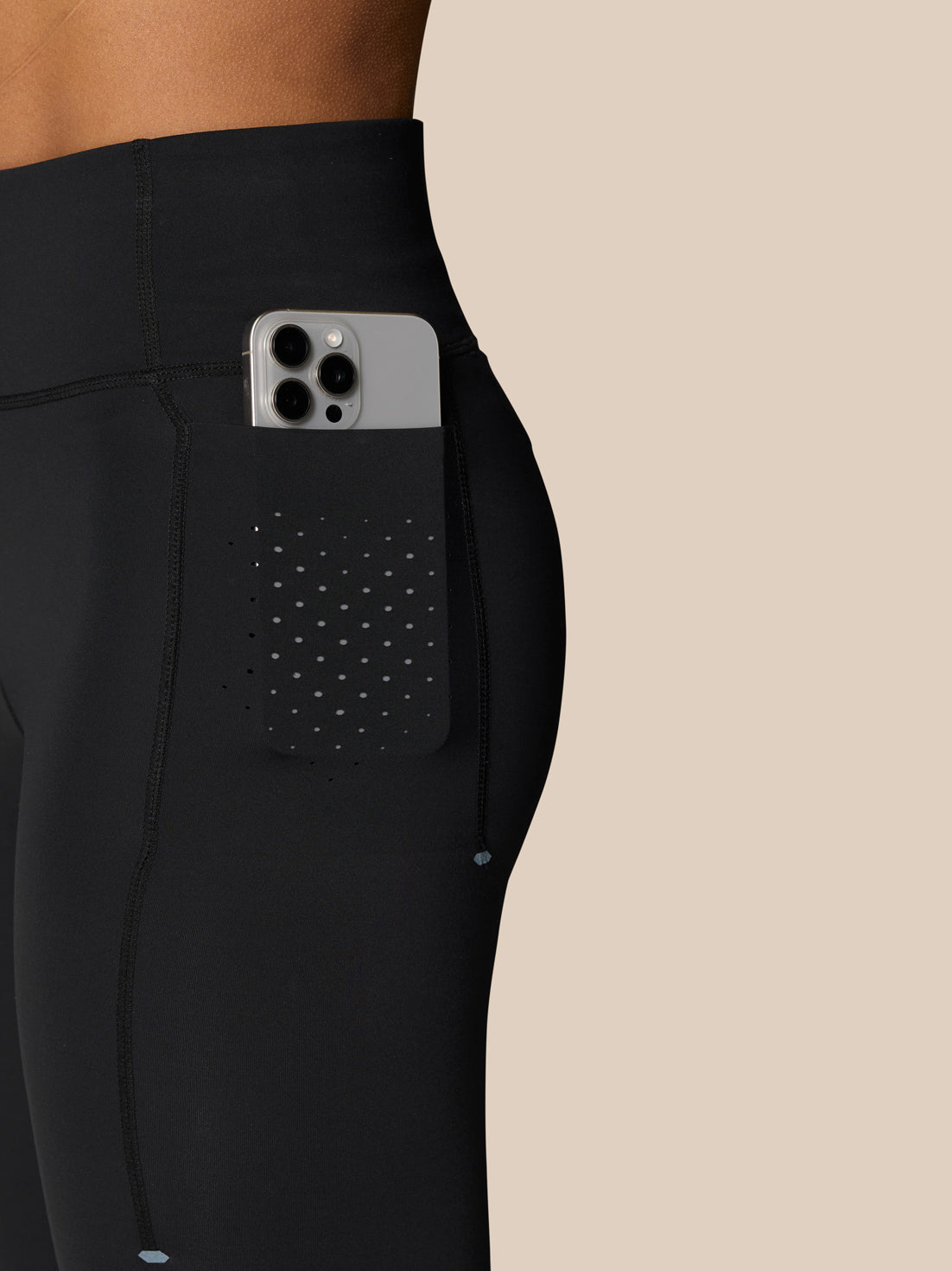 Phone tucked into the side pocket of black Zone Training Leggings showing dotted ventilation pattern