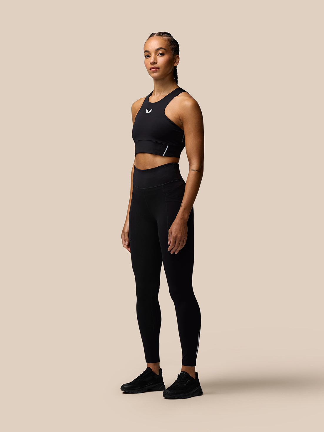 Model wearing Apex Training Leggings in black with a matching sports bra and Castore branding on the thigh