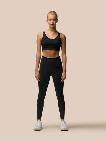 Model wearing black Flow Training Leggings with a matching sports bra and white sneakers against a beige backdrop