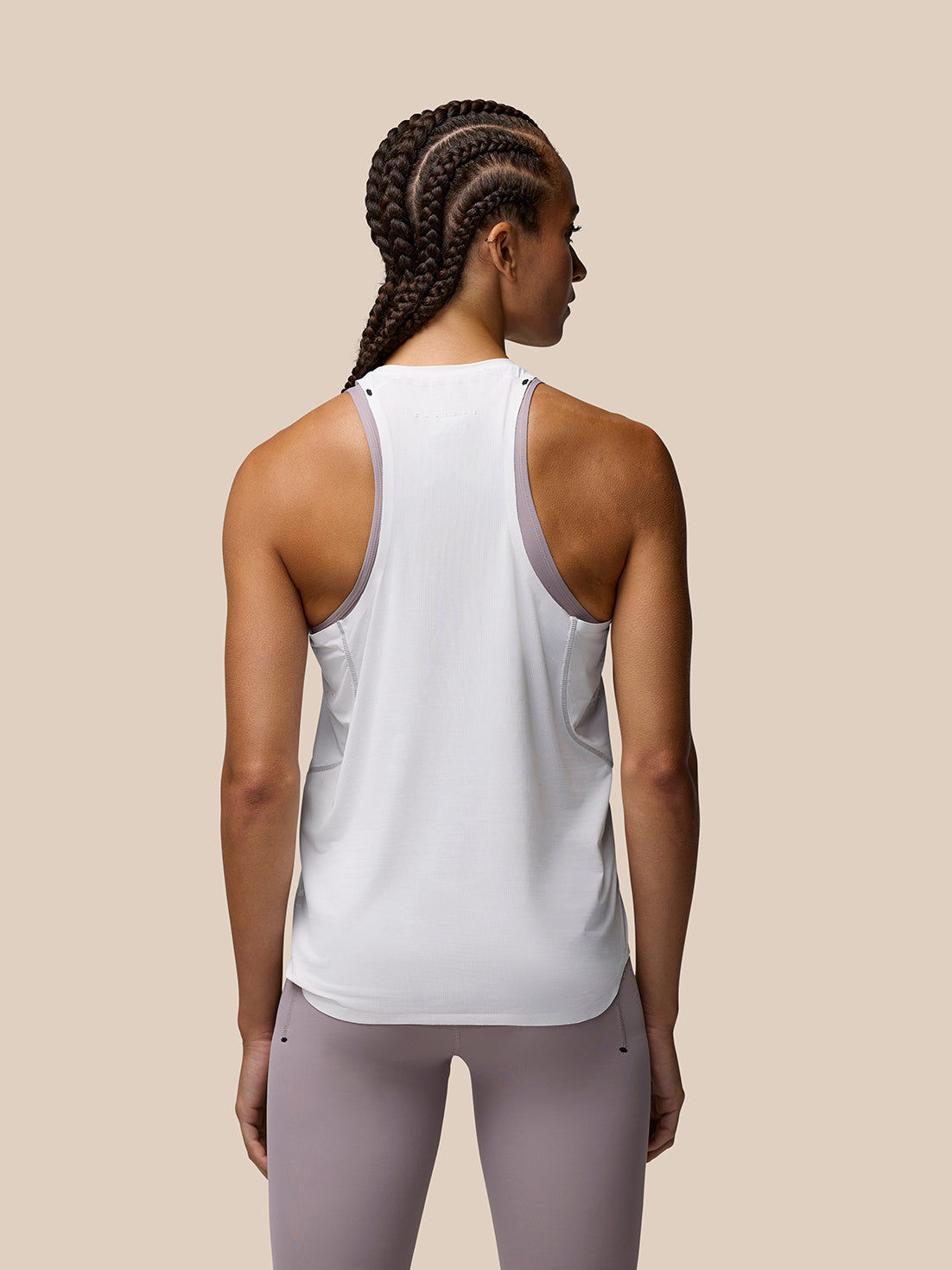 Back view of a woman wearing a white Zone Training Tank Top with lavender trim along the armholes and center back branding