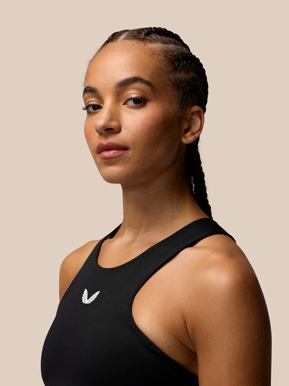 Three-quarter view of a woman in the black Apex Training Sports Bra with scoop neckline and chest logo.