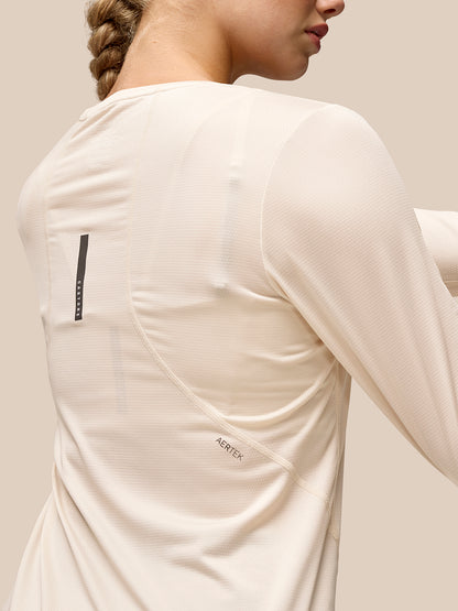 Back view of beige Flow Movement long sleeve top on a model showing a dropped back hem and back branding.