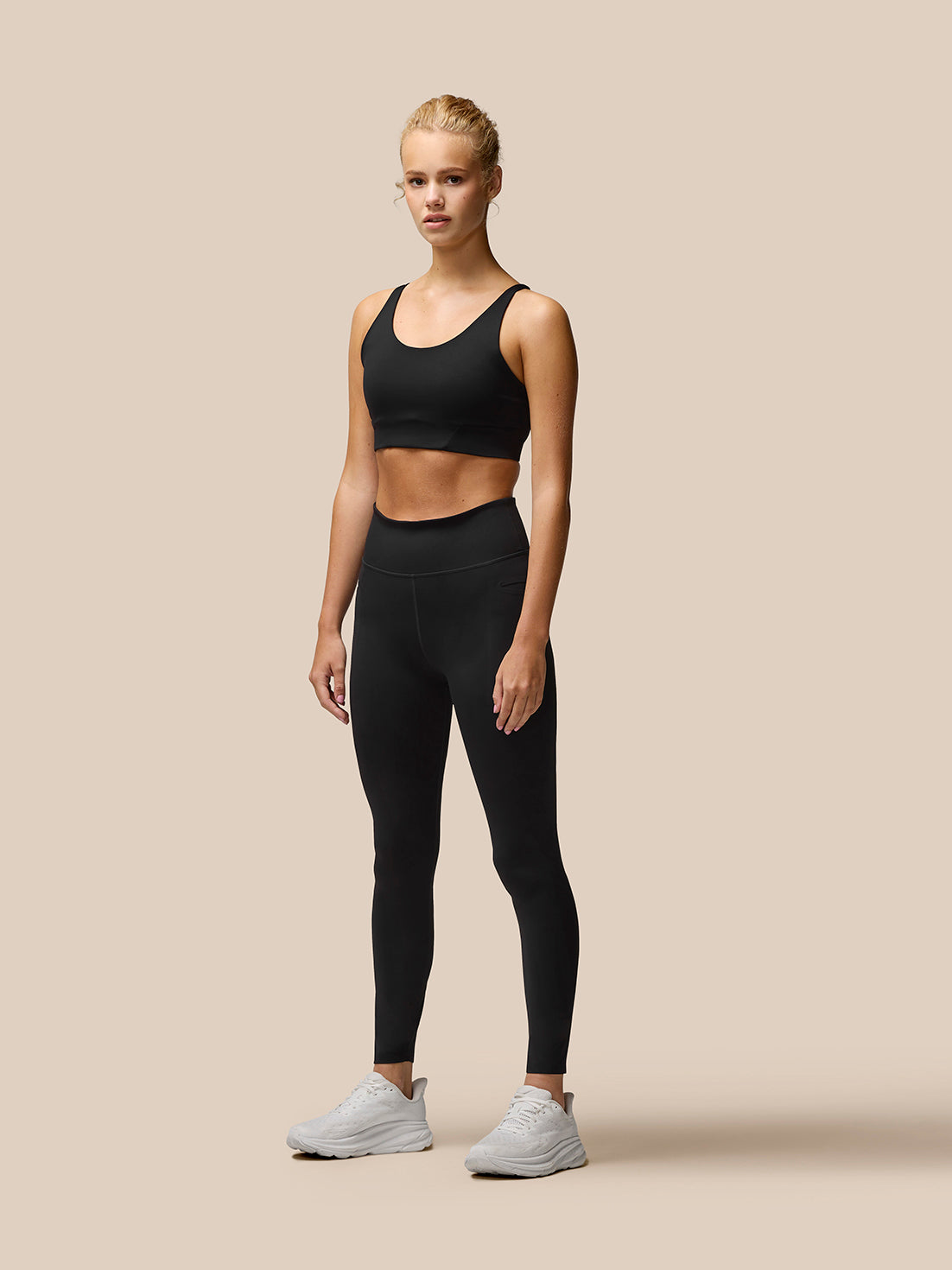 Model wearing black Flow Training Sports Bra with matching leggings and white sneakers.