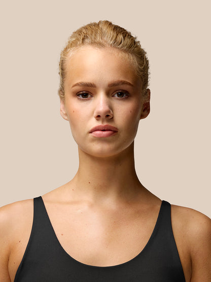 Portrait of a model wearing Flow Training Sports Bra in black with thin shoulder straps.