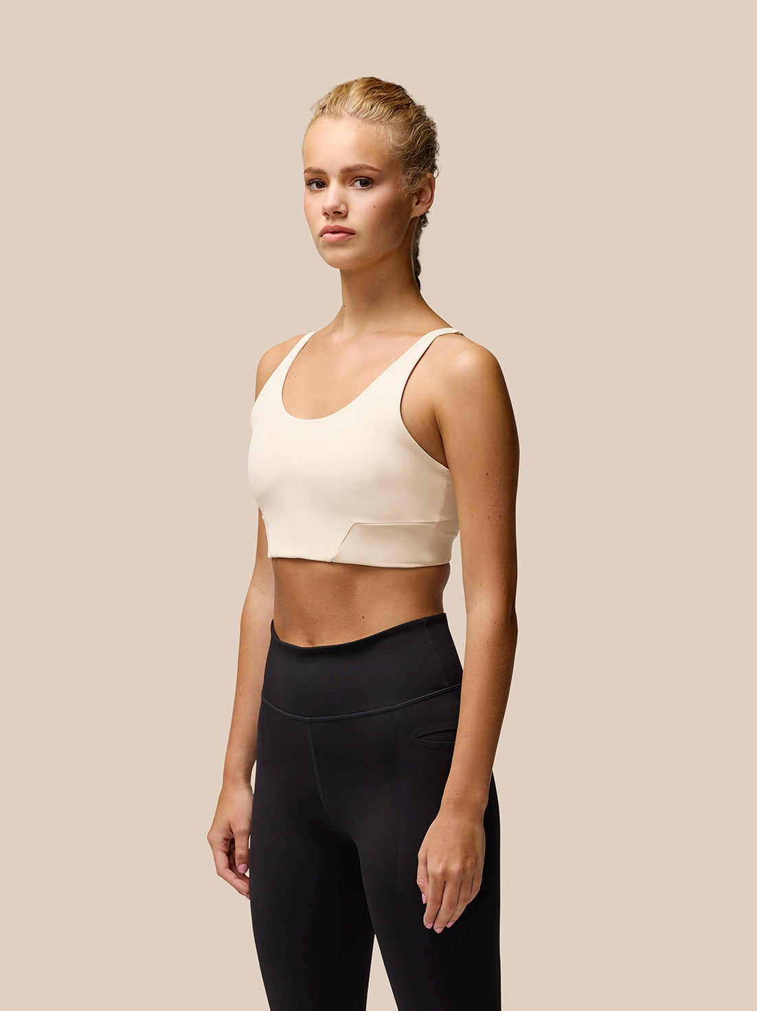 Model wearing beige Flow Training Sports Bra with cropped silhouette and black leggings
