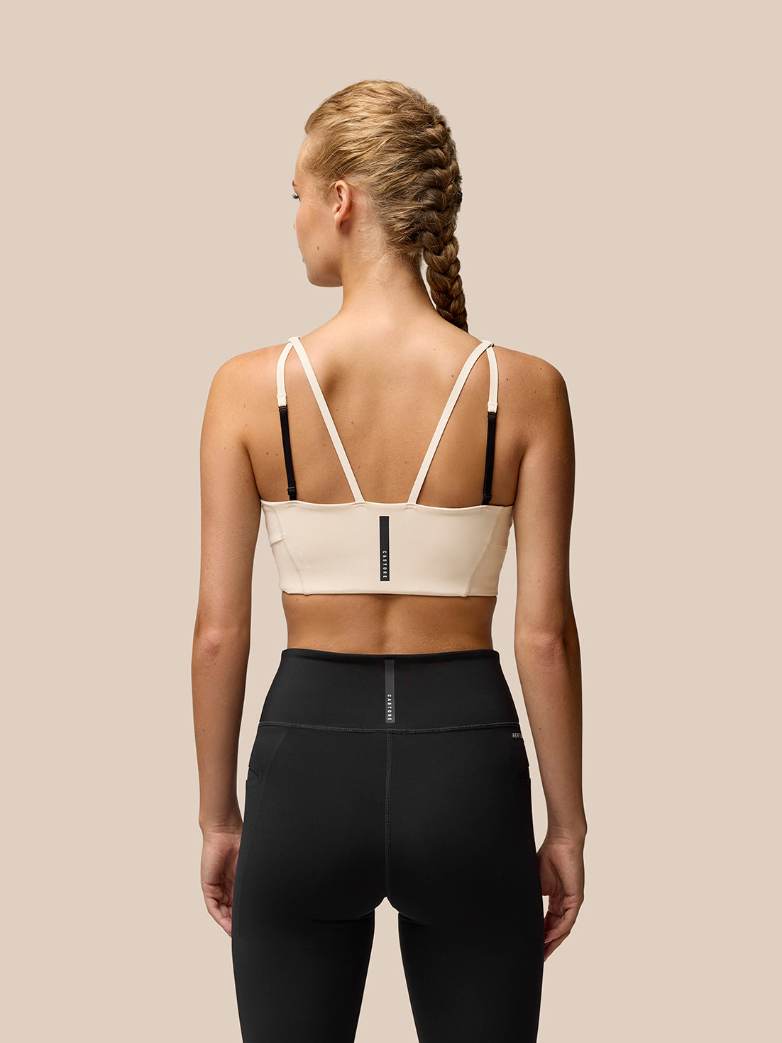 Back view of beige Flow Training Sports Bra with adjustable straps worn with black leggings