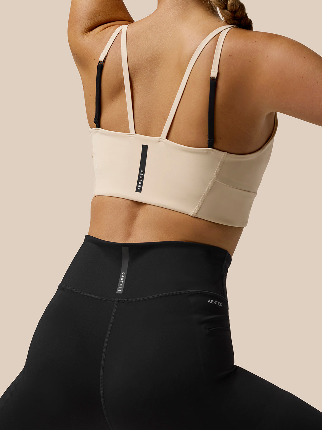 Back view of Flow Training Sports Bra beige with a multi strap back design and CASTORE branding on the back.