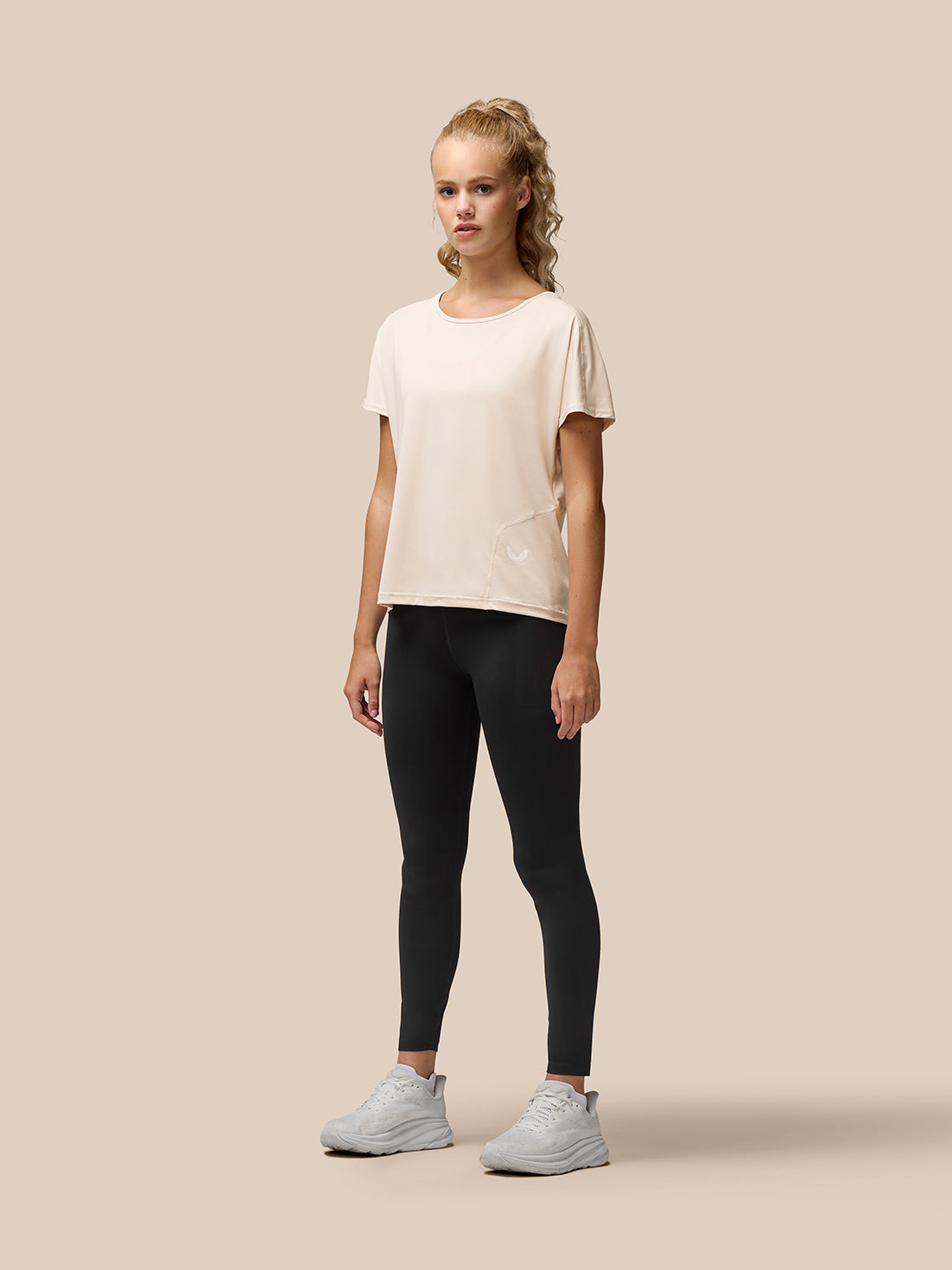 Front view of a model wearing a beige Flow Training T-Shirt with scoop neckline and curved hem, small logo at the left hem.