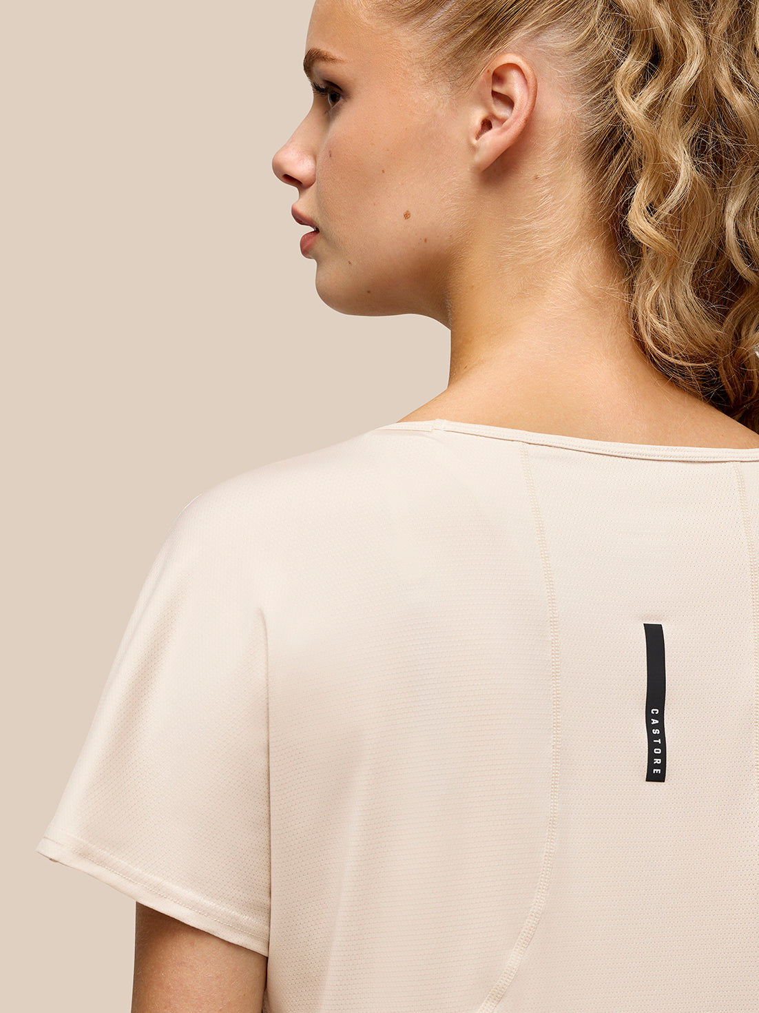 Side profile of beige Flow Training T Shirt with Castore branding on the back waist.