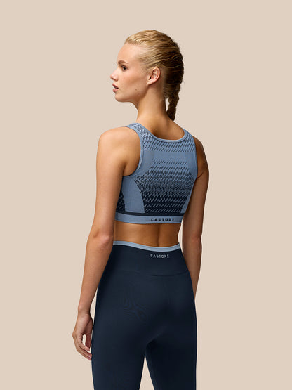 Back view of a model wearing a Dove Blue Flow Training Seamless Crop Sports Bra with a textured jacquard pattern and Castore branding on the back band