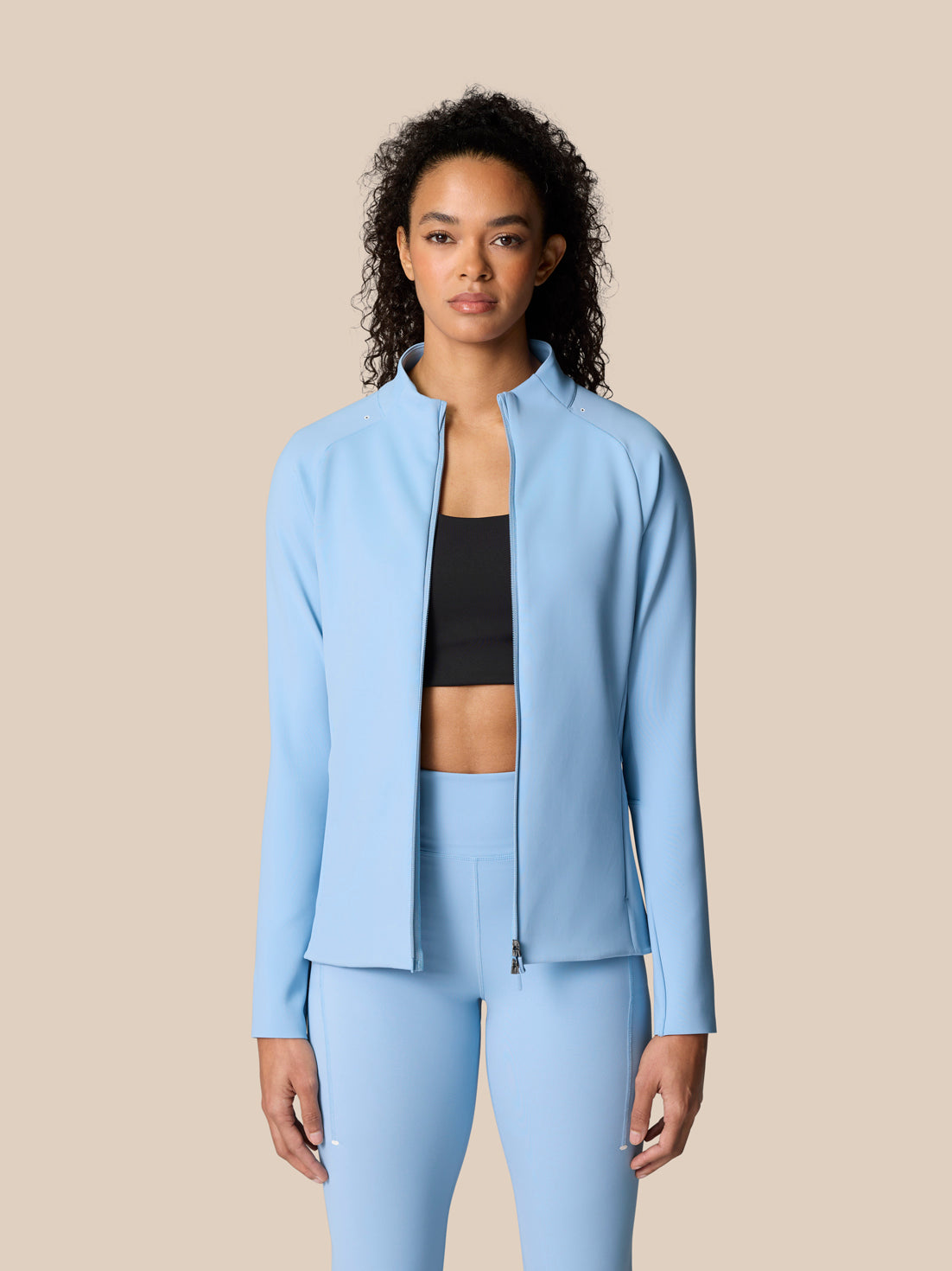 Female model wearing sky blue Zone Training Top full zip jacket with a raised collar over a black sports bra.