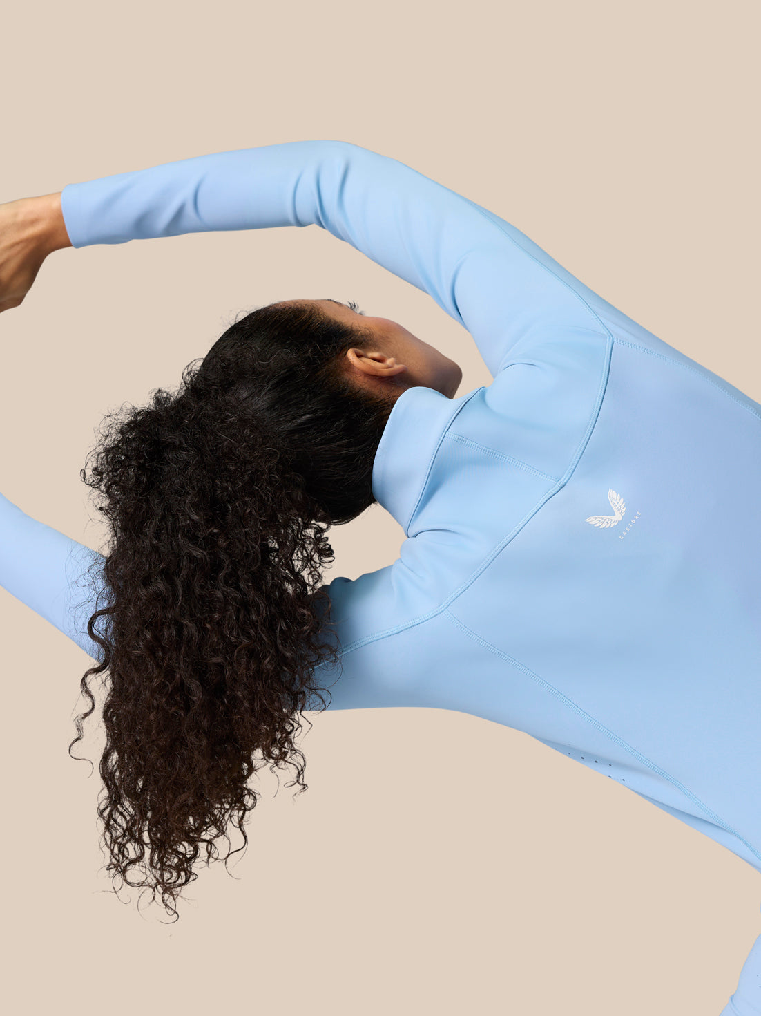 Person wearing sky blue Zone Training Top stretches with arms raised, back logo visible on the jacket.
