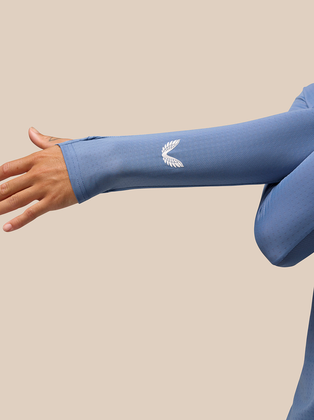Close up of model's forearm in a light blue Apex Training top showing a white logo on the sleeve.